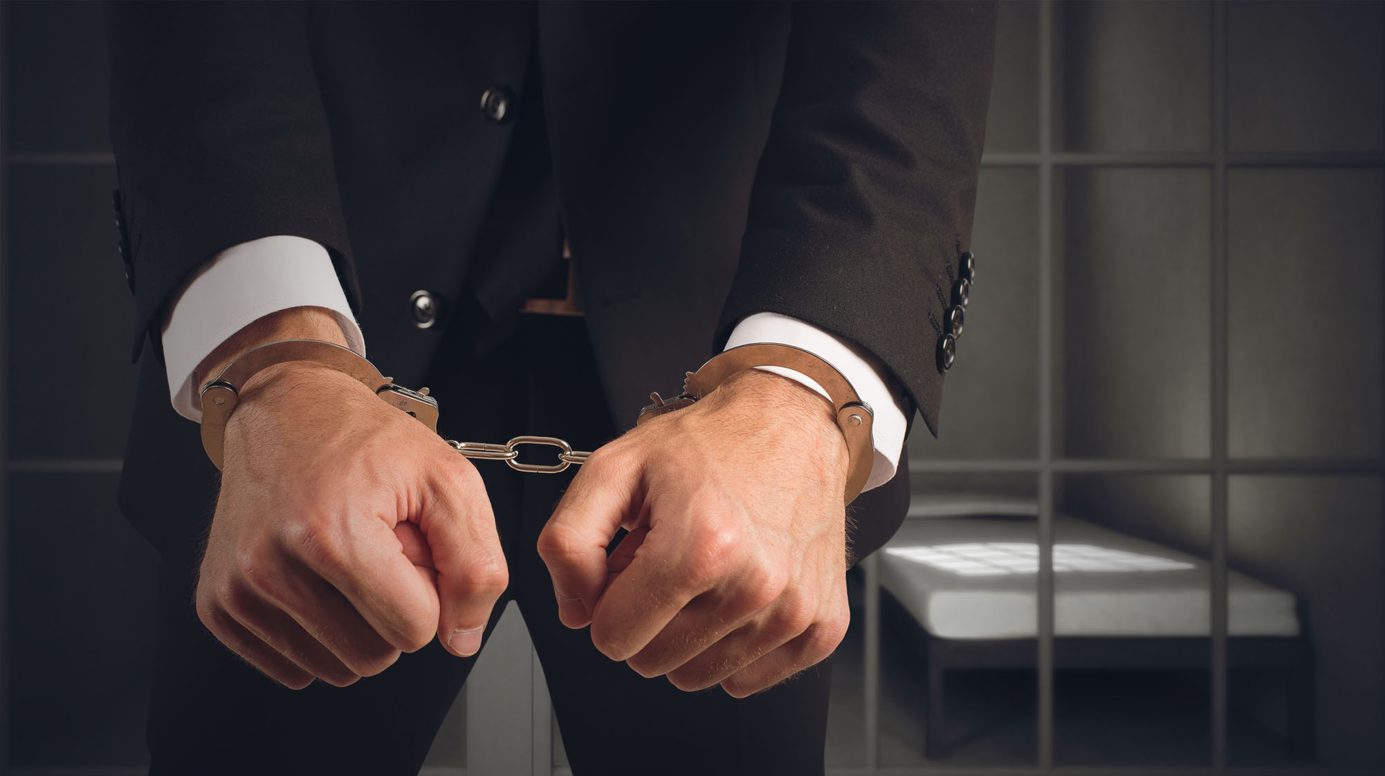 White Collar Crimes man in a business suit wearing handcuffs for being involved in a white collar crime